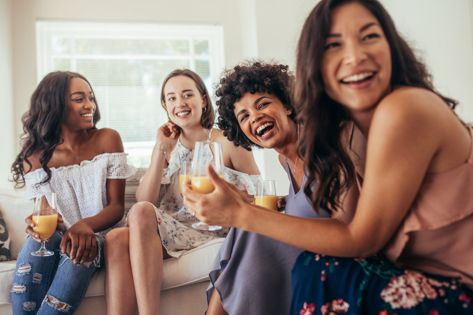 Four women enjoying a drink, laughing and sitting on a couch.